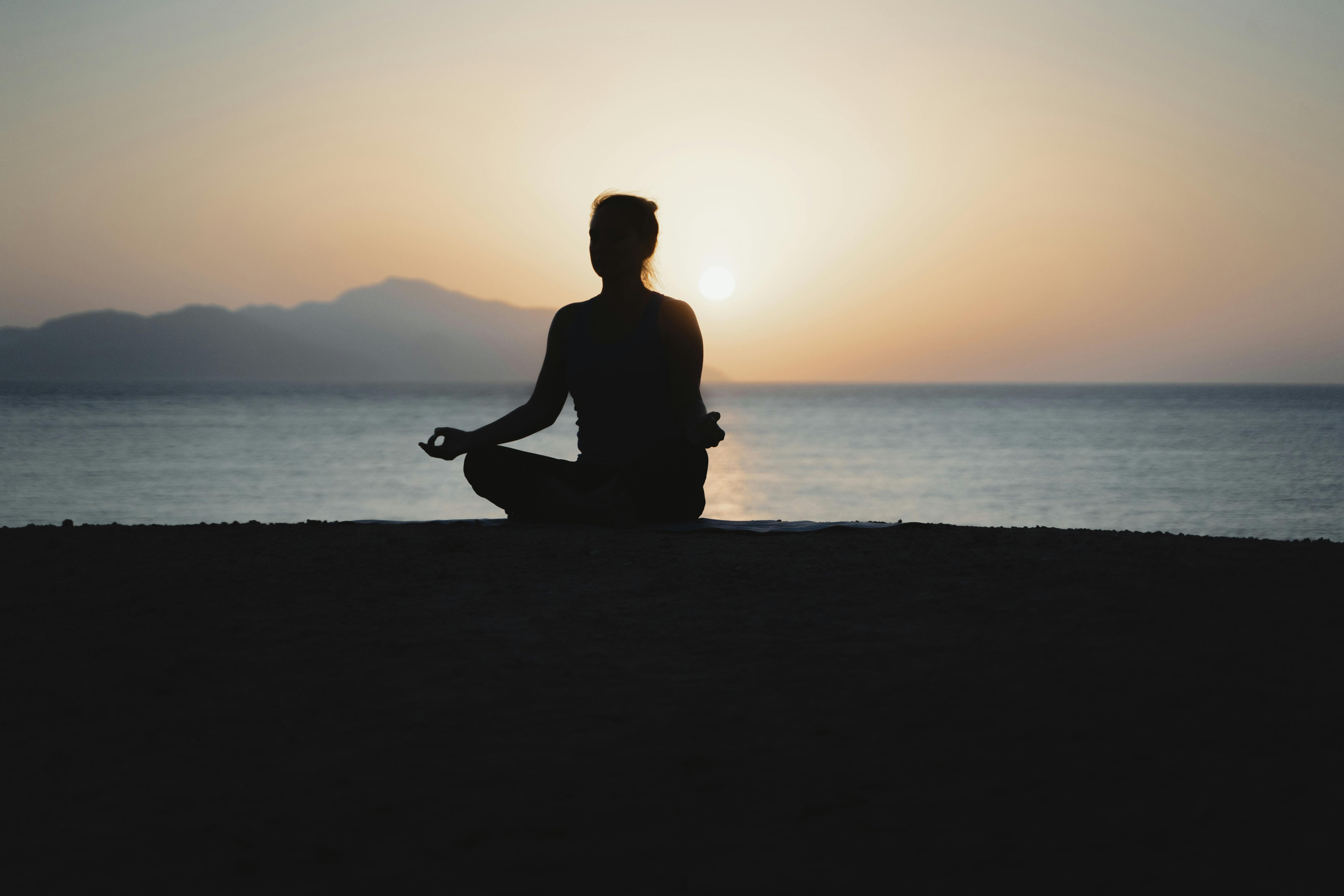 Person meditating by the ocean at sunset