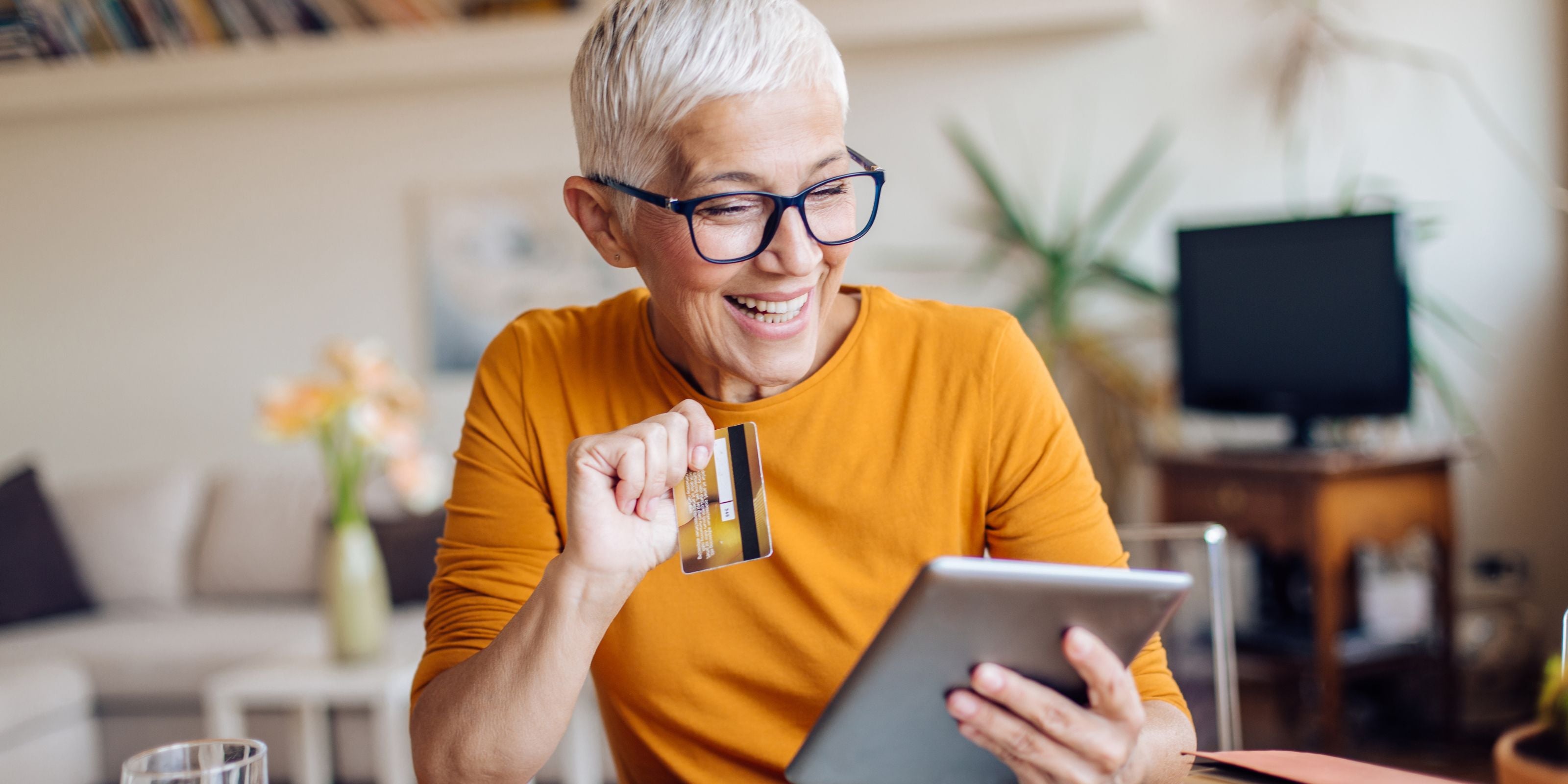 Woman in an orange sweater using a tablet in a living room.