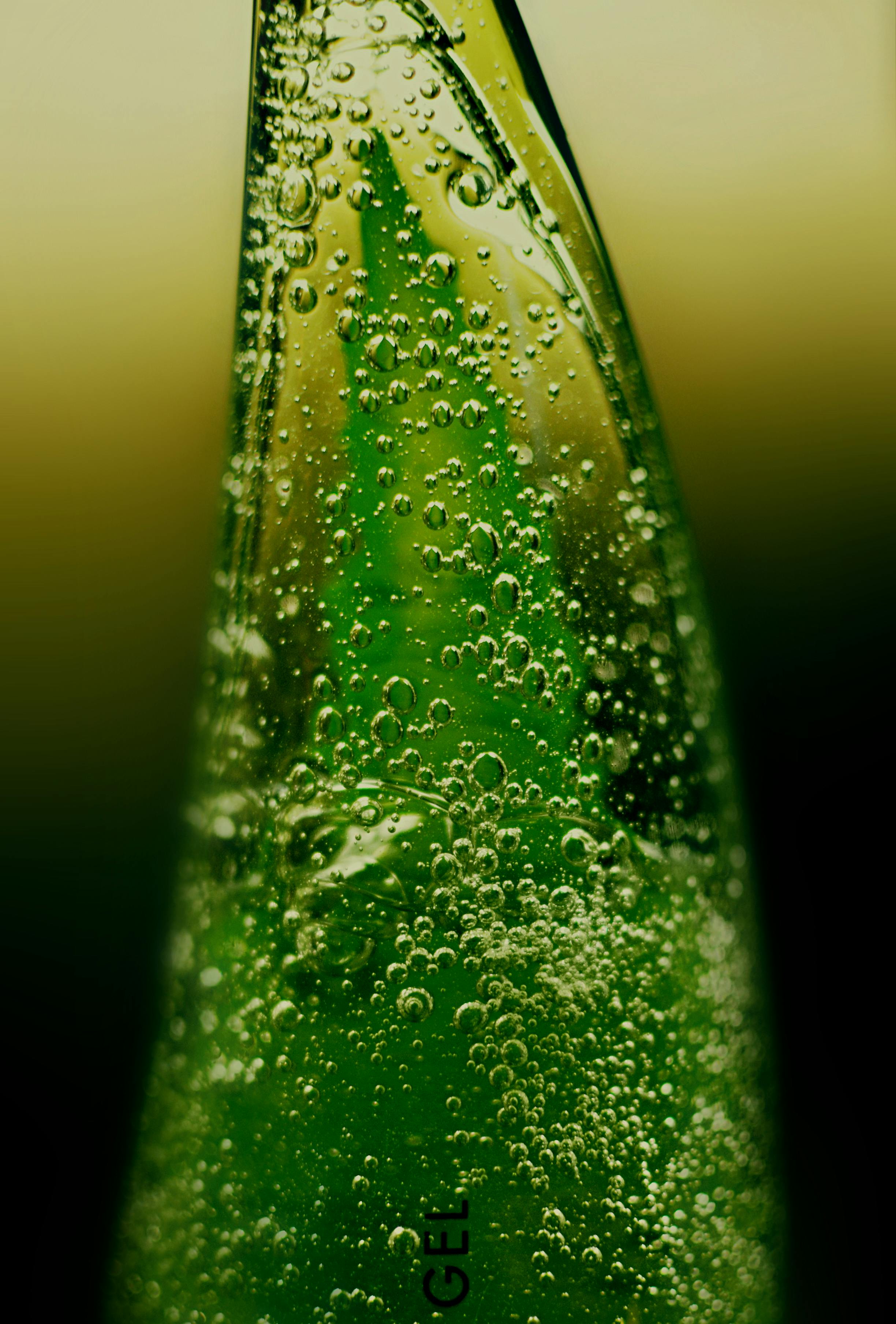 Close-up of a green glass bottle with bubbles on a blurred background